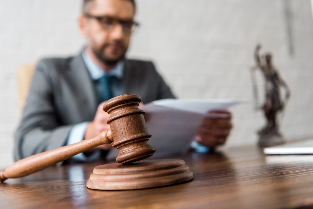 Legal Complexities of Corporate Governance Close-up view of a wooden gavel on a desk, with a judge working on legal documents in the background, featuring 411 Corporate Law and highlighting the legal complexities of corporate governance, aligned with the page's focus on corporate law.